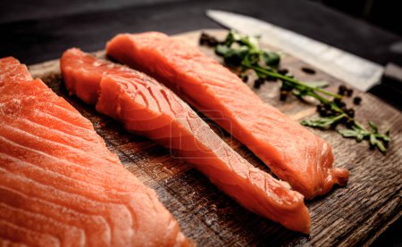 Foto de Filetes de salmón crudo con hierbas verdes en la mesa de madera con cuchillo. Filetes de pescado omega rojo para una dieta omega saludable - Imagen libre de derechos