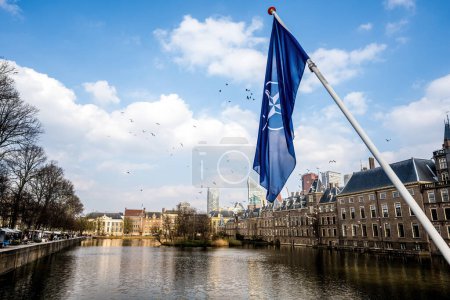 Téléchargez les photos : Drapeau de l'OTAN au centre du ciel de La Haye avec vue sur les canaux fluviaux hollandais et les bâtiments de la vieille ville. Paysage du site Hollande, - en image libre de droit