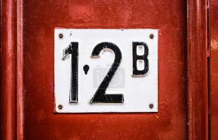 Téléchargez les photos : Panneau d'adresse sur la porte en bois du bâtiment résidentiel avec l'appartement numéro douze. Panneau d'identification de maison - en image libre de droit