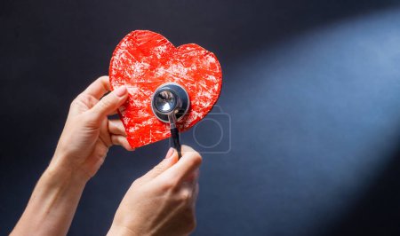 Téléchargez les photos : Main tenant coeur rouge avec stéthoscope comme symbole de charité, de santé et de soutien cardiaque médixcal. Concept de responsabilité et de bien-être - en image libre de droit