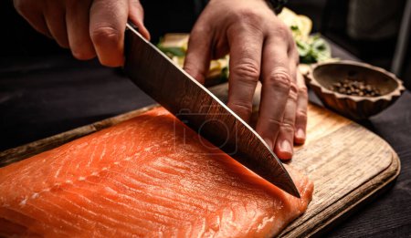 Téléchargez les photos : Sushi chef coupe le saumon cru au couteau sur une table en bois pour sashimi japonais. Cuisinier professionnel préparant truite de poisson orange fraîche - en image libre de droit