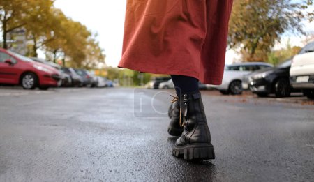 Téléchargez les photos : Jambes féminines en cuir noir Bottes Stride consciencieusement dans les rues de la ville, fille marchant après la pluie - en image libre de droit
