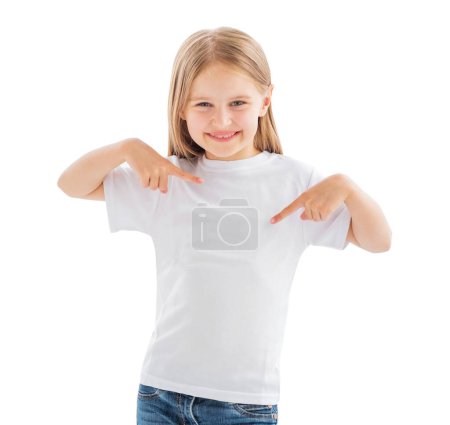 Téléchargez les photos : Jolie petite fille souriante pointant sur un t-shirt blanc blanc isolé sur un fond blanc - en image libre de droit