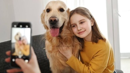 Photo for Girl hand with smartphone taking photo of golden retriever dog and preteen child kid at home. Woman mother photograph shoting pet doggy and daughter with mobile phone camera - Royalty Free Image