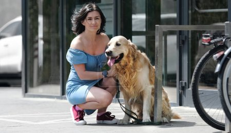 Foto de Golden retriever perro con correa y chica bonita sentado en la calle cerca del supermercado. Púrpura mascota perrito y joven mujer juntos al aire libre en la ciudad - Imagen libre de derechos