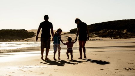 Foto de Familia feliz con silueta de niños en la puesta de sol de la playa del mar. Padre, madre e hijos caminando en la orilla del mar con la luz del sol de la noche - Imagen libre de derechos