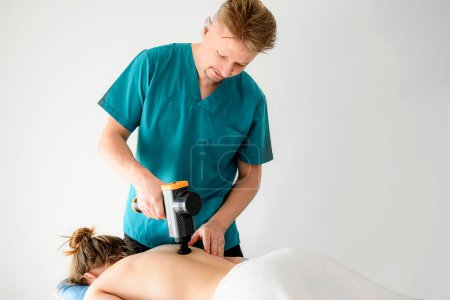 Téléchargez les photos : Masseur homme faisant massage dos à fille client à l'aide d'une machine de masseur professionnel. Soins du corps traitement thérapie procédure pour le bien-être et la relaxation dans une clinique de salon de spa avec outil spécial. - en image libre de droit
