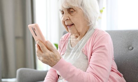 Anciana habla a través de videollamada usando Smartphone en la sala de inicio