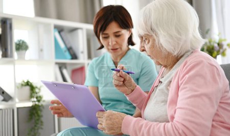 Foto de Enfermera ayudando a anciana a firmar documentos en el hogar de ancianos - Imagen libre de derechos