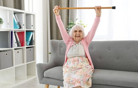 Photo for Elderly Woman Lifts Walking Cane Upwards Symbolizes Victory Over Disease - Royalty Free Image