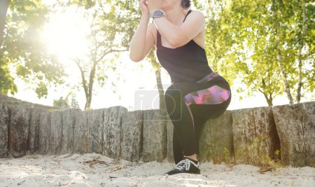 Foto de Chica de fitness haciendo sentadillas en la pierna, la cadera y la rodilla entrenamiento de los músculos articulares, recriminación al aire libre - Imagen libre de derechos