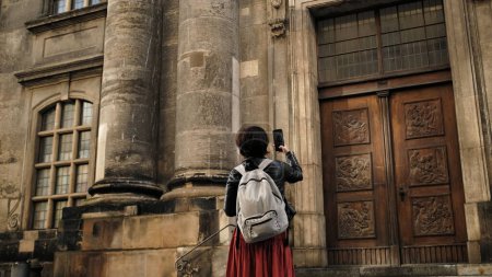 Téléchargez les photos : Promenades touristiques féminines attrayantes avec le drapeau d'Allemagne dans le centre historique de Dresde, prenant des photos d'endroits touristiques - en image libre de droit