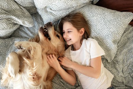 Téléchargez les photos : Petite fille mignonne jouant avec Golden Retriever chien au lit - en image libre de droit