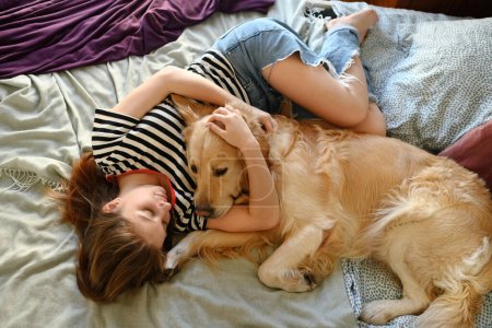 Foto de Linda chica jugando con Golden Retriever perro en la cama - Imagen libre de derechos