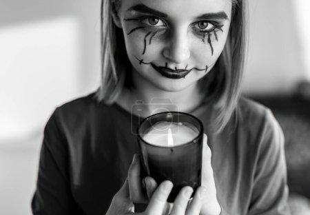 Foto de Chica preadolescente con espeluznante maquillaje de Halloween posando en la cámara con vela de iluminación. Retrato infantil para vacaciones espeluznantes en blanco y negro. - Imagen libre de derechos