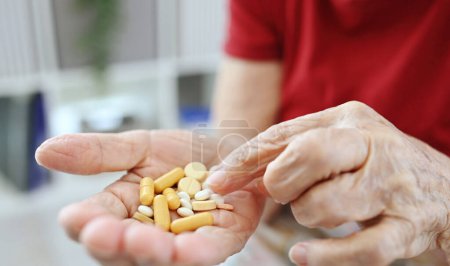 Photo for Elderly Woman Counts Pills And Capsules In Her Palm, Medical Drugs And Vitamins For Older People - Royalty Free Image