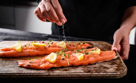 Téléchargez les photos : Salage en chef avec une pincée de sel cru truite rouge poisson pour la cuisson à la cuisine - en image libre de droit