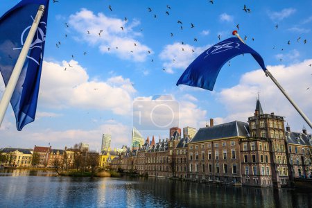 Foto de Ondeando la bandera de la OTAN en el centro del cielo de La Haya con canales de río holandés y vistas a edificios antiguos de la ciudad. Paisaje de Holanda, - Imagen libre de derechos