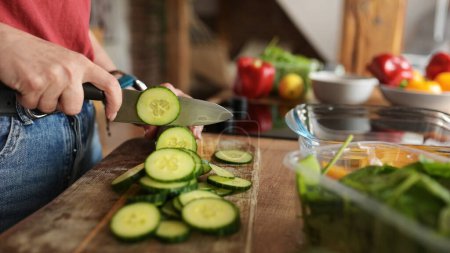 Foto de Mujer cortando pepinos en una tabla de cortar para una cena de verduras saludables - Imagen libre de derechos