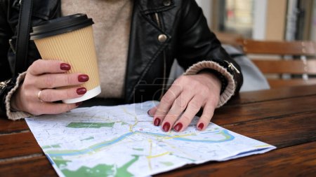 Foto de Elegante turista femenina comprueba la ruta turística de la ciudad en el mapa mientras toma café en el café de la calle - Imagen libre de derechos