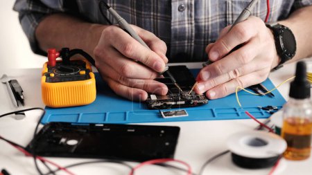 Téléchargez les photos : Maître technicien dans un centre de service de réparation d'électronique répare un smartphone, démonter le téléphone - en image libre de droit