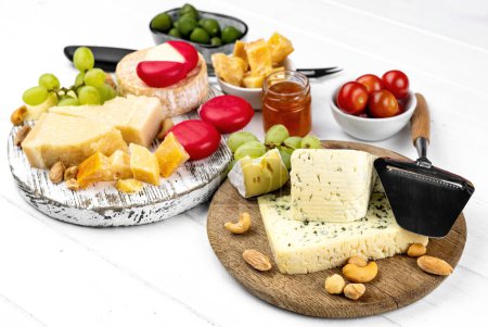 Téléchargez les photos : Différents types de fromage servi avec des olives vertes, des tomates et du raisin pour une nutrition gastronomique. Parmesan bio et brie à la charcuterie au miel - en image libre de droit