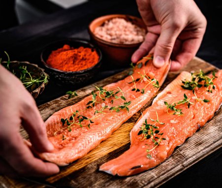 Photo for Chief hands put fresh trout salmon filet with herbs on wooden board. Omega orange fish with rosemary for healthy nutrition - Royalty Free Image