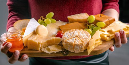 Photo for Girl holding different kinds of cheese and honey on wooden table in hands closeup. Woman with organic parmesan and brie set french delicatessen - Royalty Free Image