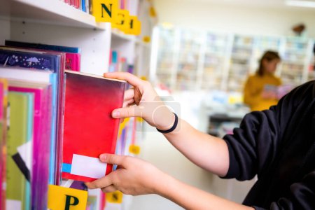 Photo for Girl taking a red book from shelves in the light school library. - Royalty Free Image