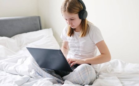 Foto de Enfocado niña haciendo su tarea en línea en una cama grande en la mañana - Imagen libre de derechos