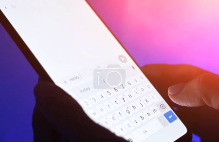Foto de Girl typing message on a smartphone against blue background. Close up viwe of white sceen. - Imagen libre de derechos