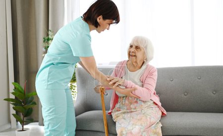 Téléchargez les photos : Infirmière Mains Canne à la femme âgée et l'aide à se déplacer dans la chambre dans une maison de soins infirmiers - en image libre de droit