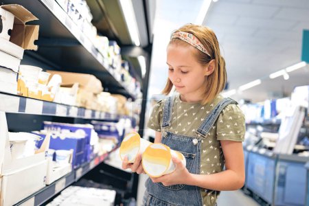 Foto de Niña bonita eligiendo yogur en la tienda de supermercados. Hermosa niña preadolescente femenina que busca productos lácteos en la tienda de comestibles - Imagen libre de derechos