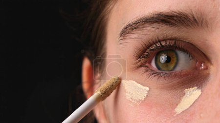Foto de Primer plano de una chica aplicando ocultador bajo sus ojos y maquillaje en sus párpados - Imagen libre de derechos