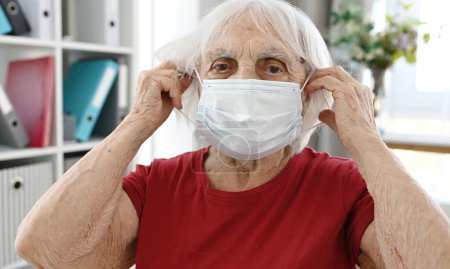 Foto de Mujer mayor se pone máscara médica protectora en la cara - Imagen libre de derechos