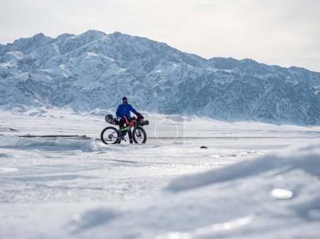 Ein Mann ist mit einem Fatbike auf dem Eis eines zugefrorenen Bergsees unterwegs. Reisen im Winter. Extreme expedition