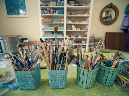 In the workshop of a ceramic artist. In the foreground on the table are special glasses with tools. Stacks, scallops, pencils and brushes.