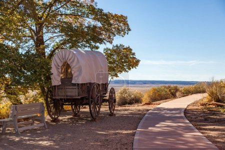 Ein alter Planwagen aus Holz am historischen Standort des Pipe Springs National Monument neben einem Fußweg und einem Blick auf die offene Wüste in der Ferne.