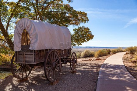 Ein alter Planwagen aus Holz am historischen Standort des Pipe Springs National Monument neben einem Fußweg und einem Blick auf die offene Wüste in der Ferne.
