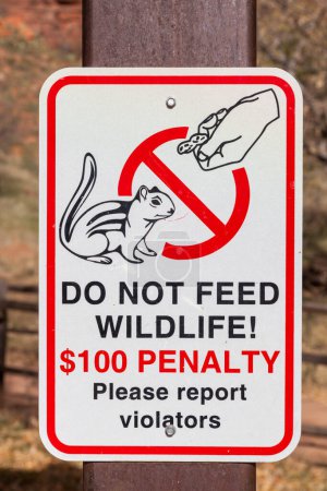 Un letrero blanco con texto negro y rojo advirtiendo a la gente que no pague la vida silvestre publicada en el área de Narrows del Parque Nacional Zion, Utah.