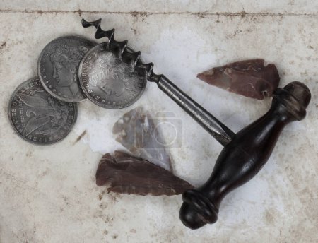 Foto de Colección vintage única de sacacorchos antiguos, puntas de flecha americanas nativas y monedas de plata en dólares sobre fondo de papel fundido en vista de cerca - Imagen libre de derechos