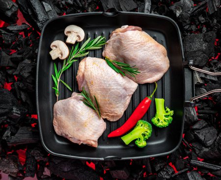 Téléchargez les photos : Raw chicken thighs in a pan with vegetables and spices stand on a hot barbecue grill. Organic meat - en image libre de droit