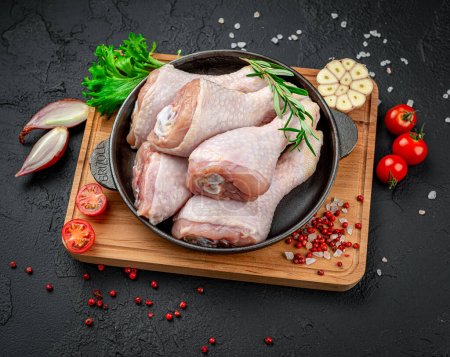 Fresh chicken drumsticks, legs with ingredients for cooking in a frying pan. Organic poultry meat. Black background. Top view