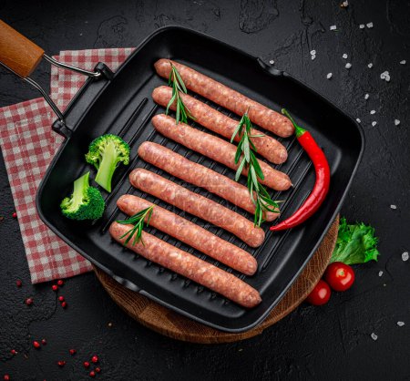 Téléchargez les photos : Raw meat sausages on a square grill pan, with herbs and spices. Munich sausages - en image libre de droit