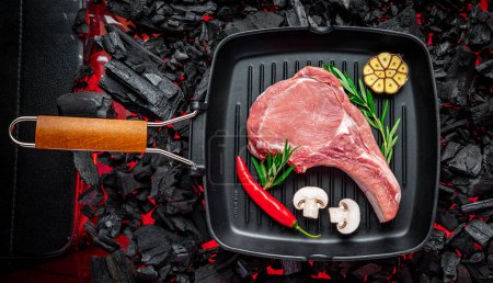 Téléchargez les photos : Raw beef steak on the grill pan, on burning charcoal barbeque - en image libre de droit