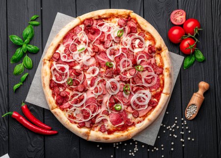 Téléchargez les photos : Pizza épicée avec jambon, saucisse, jalapeno poivrons et oignons. Pizza italienne sur fond sombre. Photo de pizza pour menu - en image libre de droit