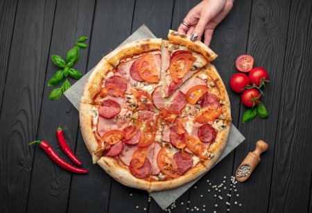 Téléchargez les photos : Pizza italienne avec jambon, saucisse, champignons, tomates et oignons. Pizza italienne sur fond sombre. Photo de pizza pour menu - en image libre de droit