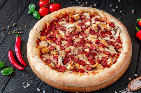 Téléchargez les photos : Grande et savoureuse pizza avec différents types de viande. Pizza italienne aux saucisses, poulet et champignons - en image libre de droit