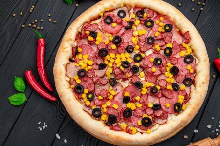 Téléchargez les photos : Pizza savoureuse et grande avec différents types de viande. Pizza aux saucisses, jambon, maïs et olives. Vue de dessus de pizza chaude. - en image libre de droit