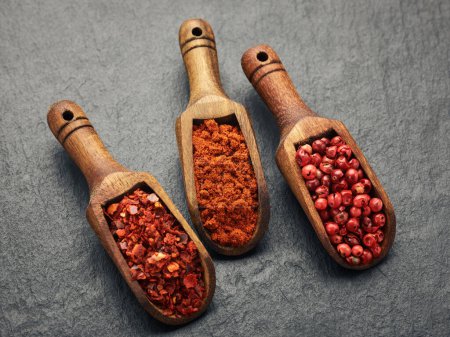 Foto de Pimienta roja, pimentón, especias de pimienta en cucharas de madera sobre la superficie de piedra negra - Imagen libre de derechos